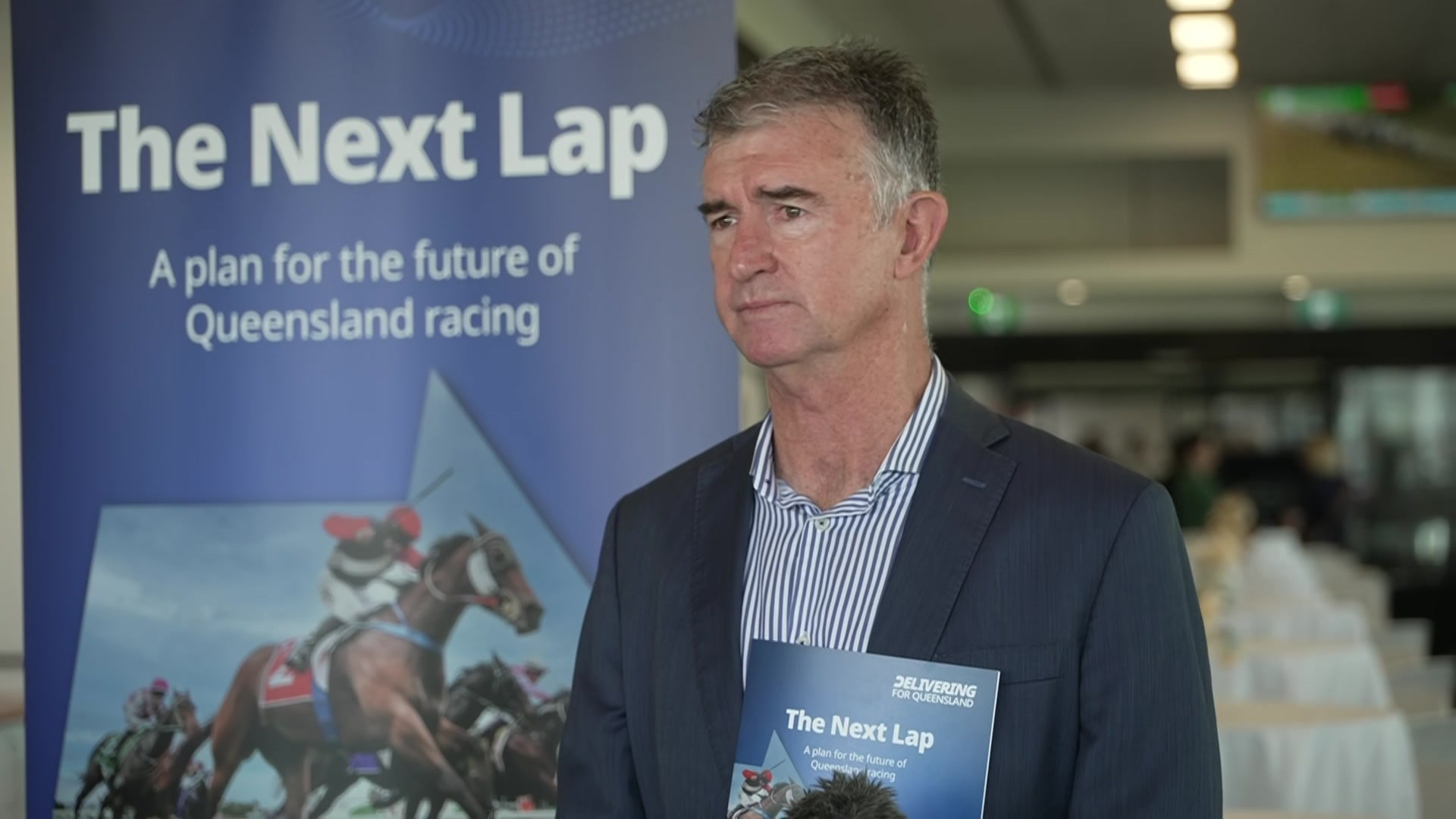 Un hombre de traje sostiene un informe titulado “ "la siguiente ronda"