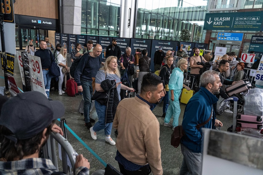 A crowd of people arrive in Turkey at an airport gate. 