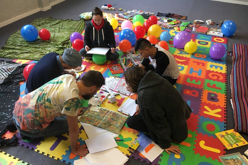 Adults sitting on the ground drawing and colouring in