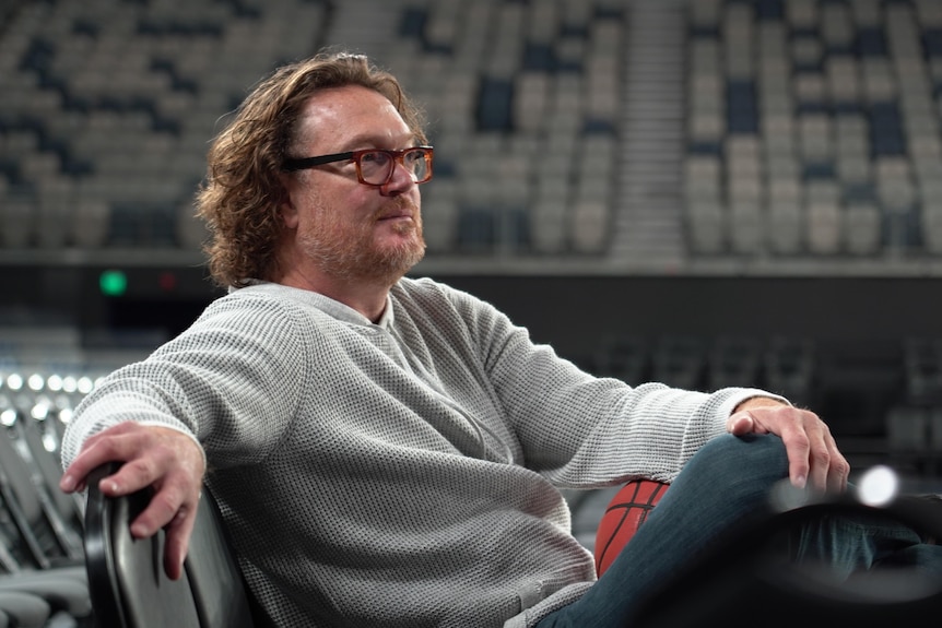 a man looks into the distance sitting on the floor of an empty basketball stadium