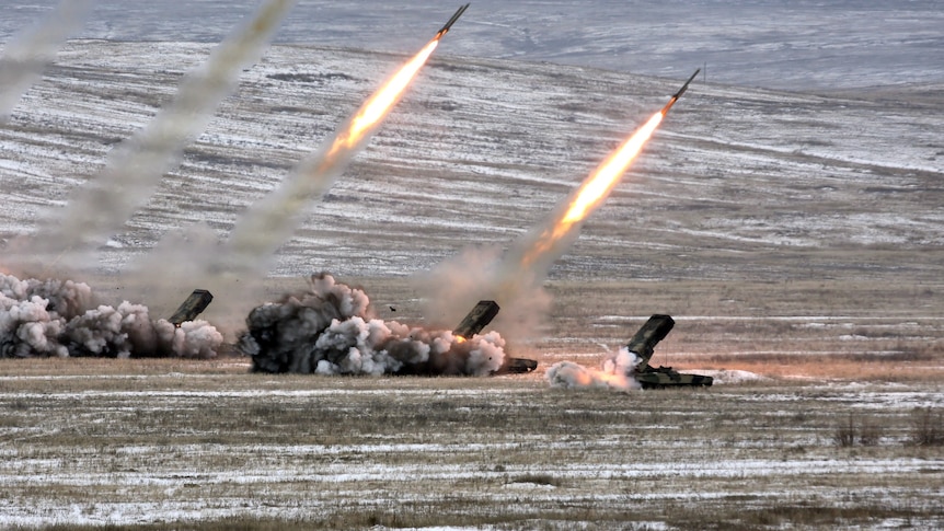 Rockets with long flaming tails fly through the air, with billowing clouds of black smoke wafting along the ground near tanks.