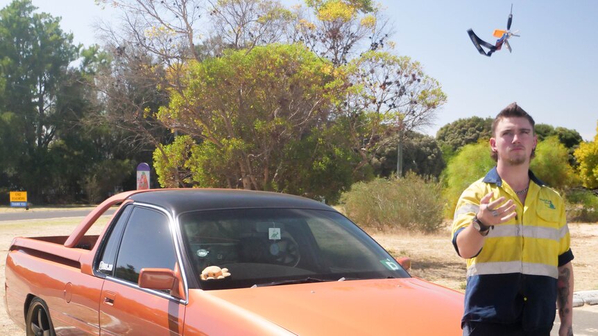 A man standing in front of a holden commodore ute throwing keys in the air