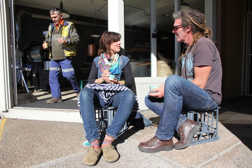 Patrons sit outside a Port Kembla cafe on milk crates chatting.