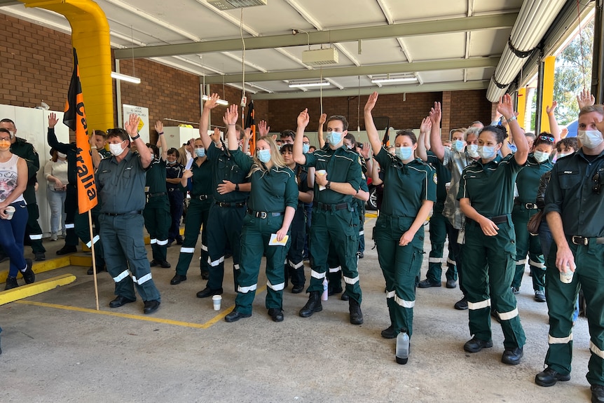 A group of paramedics in uniform with their arms raised in a vote.
