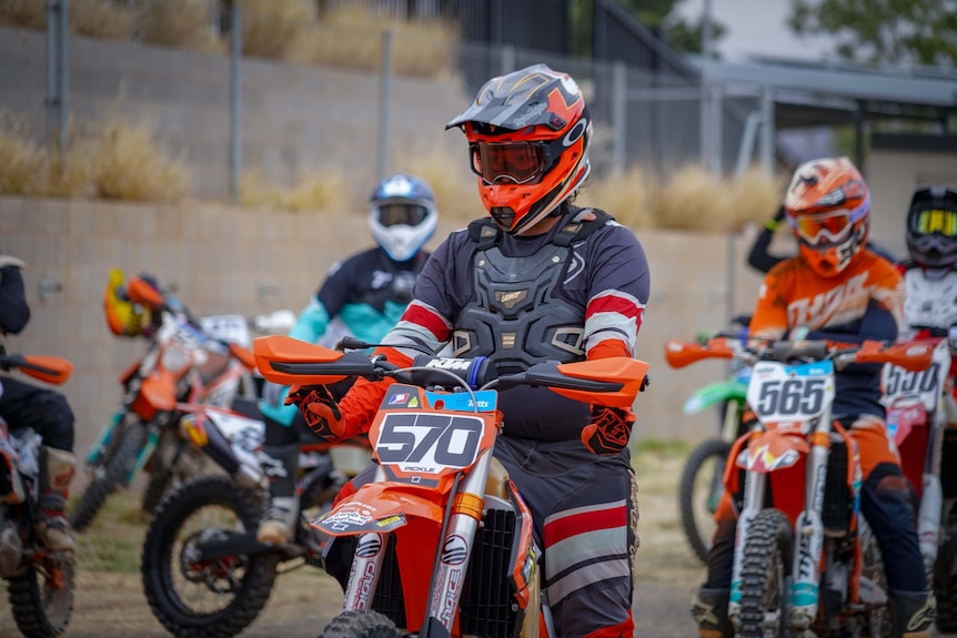 People on dirt bikes line up at a race start line.
