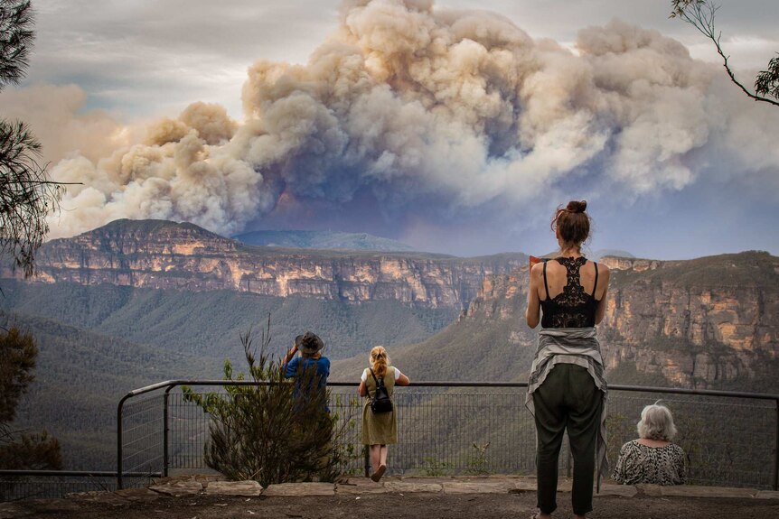 people watching large smoke plumes from a mountain lookout