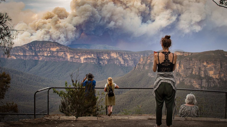 people watching large smoke plumes from a mountain lookout