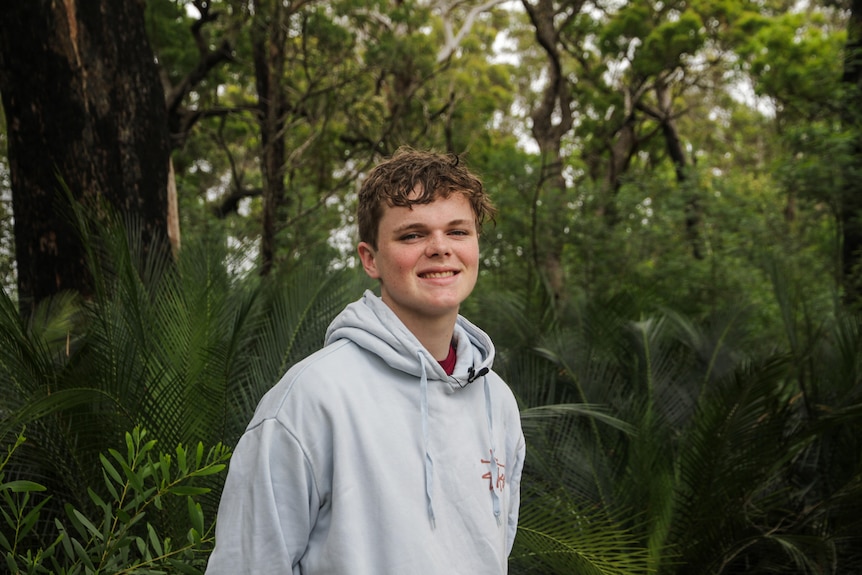 A young man wears a hoodie and stands by some bushland