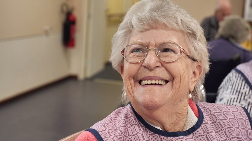 An elderly woman in spectacles smiles broadly
