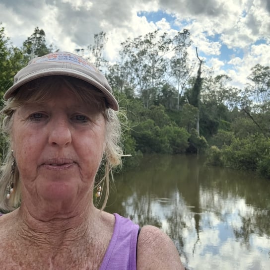 Woman in cap and purple shirt takes selfie in front of flooded road 