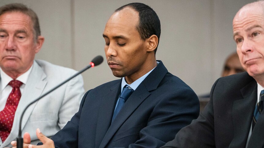 Mohamed Noor sentenced sits with his eyes closed, with lawyers sitting either side of him inside a court room