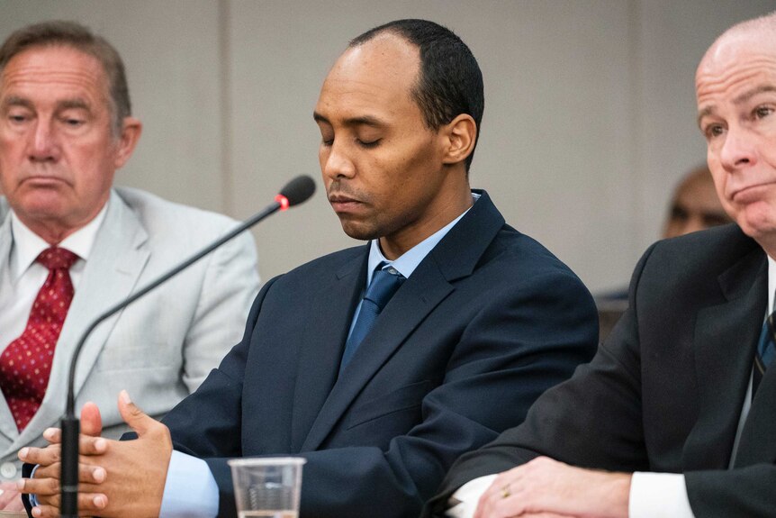 Mohamed Noor sentenced sits with his eyes closed, with lawyers sitting either side of him inside a court room