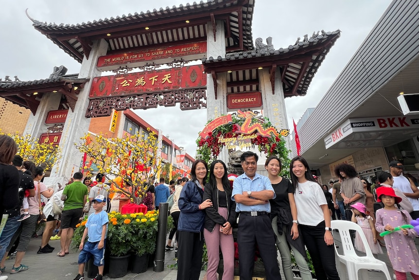 A family of five - a mum and dad and three adult daughters - stand in front of a Chinese New Year arch.
