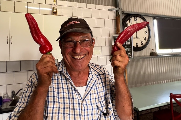 A man holding two large chillies.