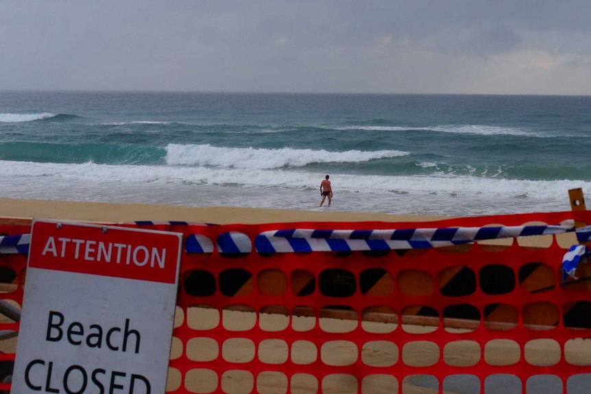 A man enters the water with a closed beach sign in the foreground at Surfers Paradise beach