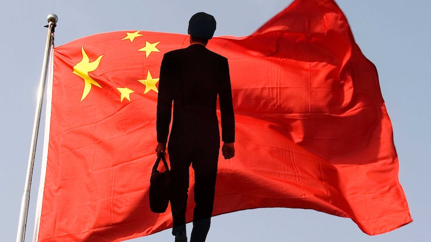 The silhouette of a businessman standing before a Chinese flag.