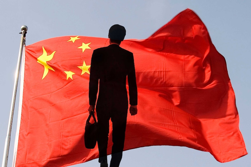 The silhouette of a businessman standing before a Chinese flag.