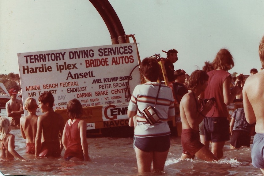 A group of people stand in knee-deep water around a vehicle.