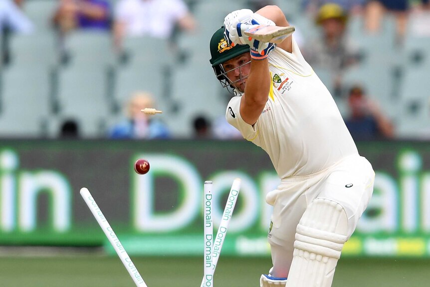 Aaron Finch plays a shot but misses the ball, which has split the stumps behind him