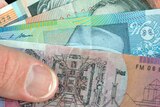 A hand holds an array of Australian dollar notes