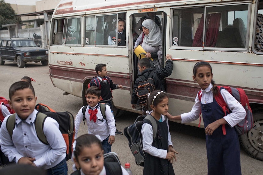 Iraqi school kids wearing a uniform board a school bus.