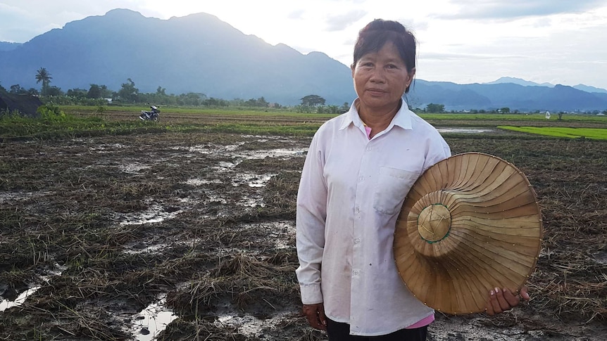 Thai rice farmer Mae Bua Chaicheun stands in a field holding a hat.