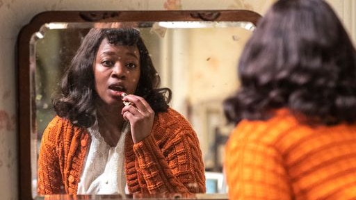 A black woman in front of a mirror applying lipstick