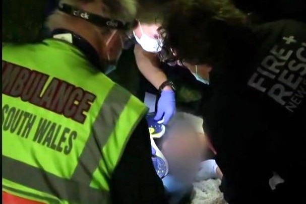 A video still showing a teenager, whose face is blurred, being treated by paramedics.