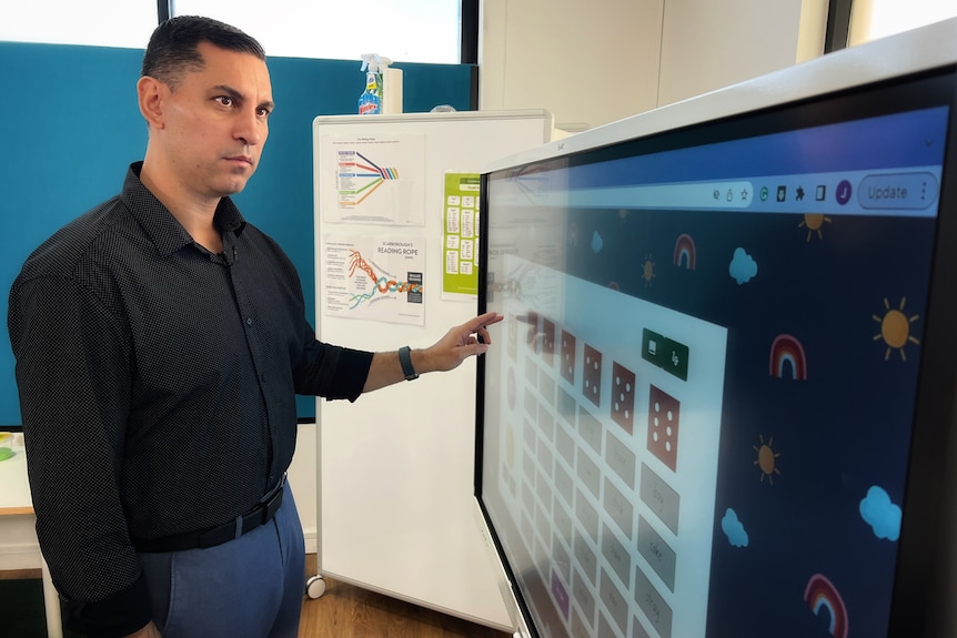 Man with dark hair wearing a black collared shirt tapping a large touch screen. 