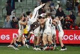 Port Adelaide AFL players pile on top of each other in the rain at the MCG after winning a game after the siren.
