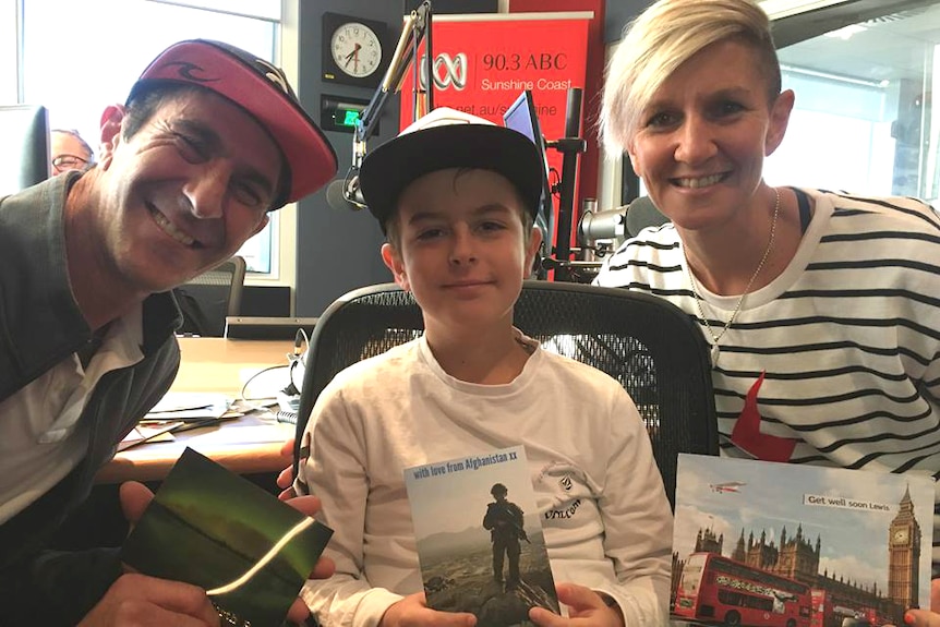 Dad, young boy and aunty in a radio studio, smiling and holding postcards.