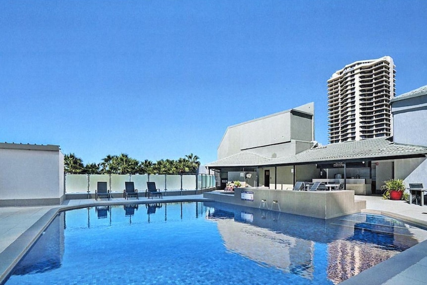 A blue-tinted swimming pool on an apartment hotel rooftop.