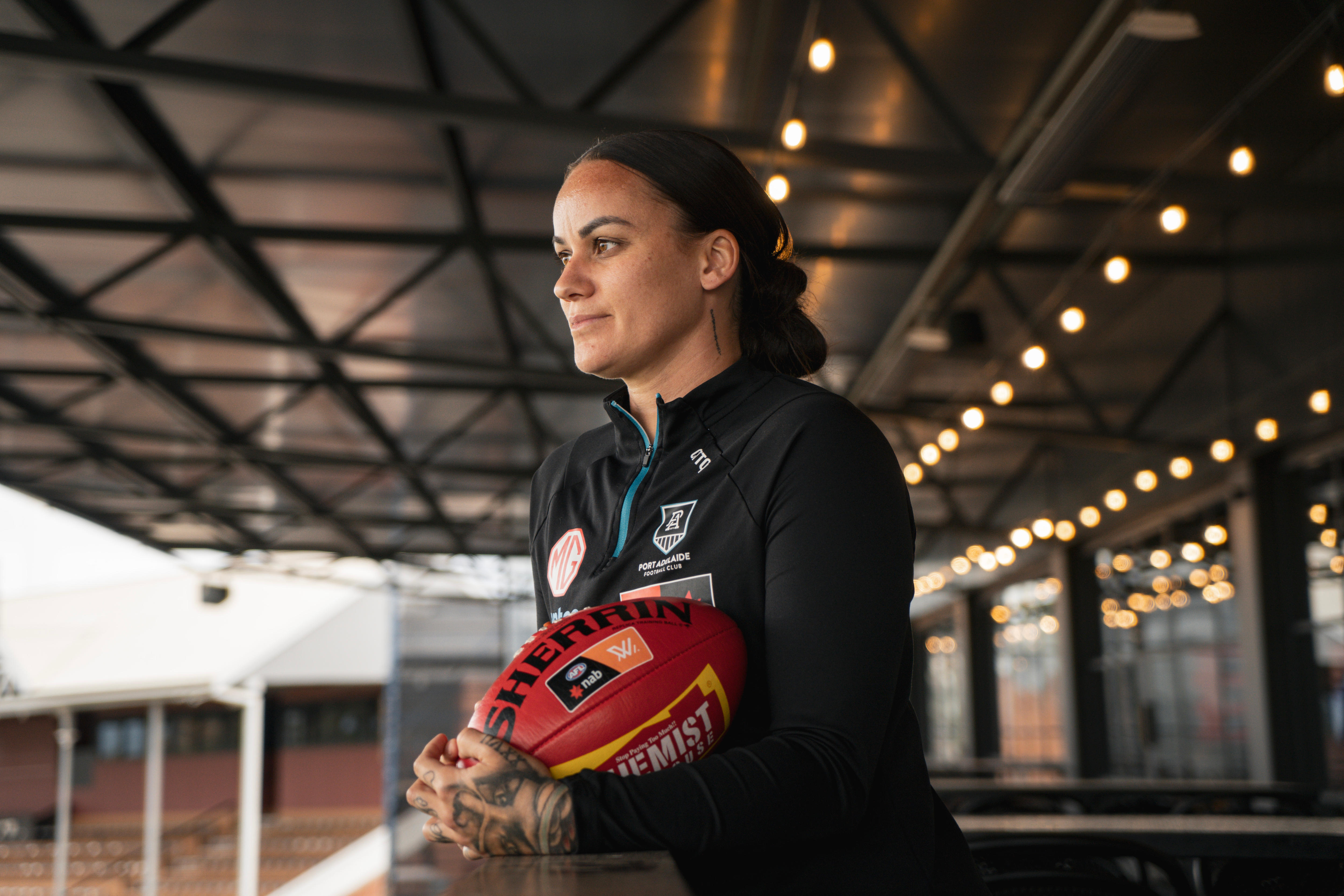 Gemma Houghton holds a footy while leaning on a railing in the stands looking away