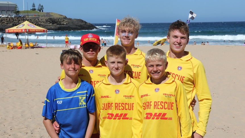 six teenagers in life saving jumpers on a beach in front of patrolled area