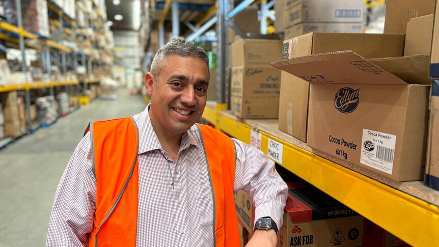 A man smiling leaning up against a shelf in a food warehouse
