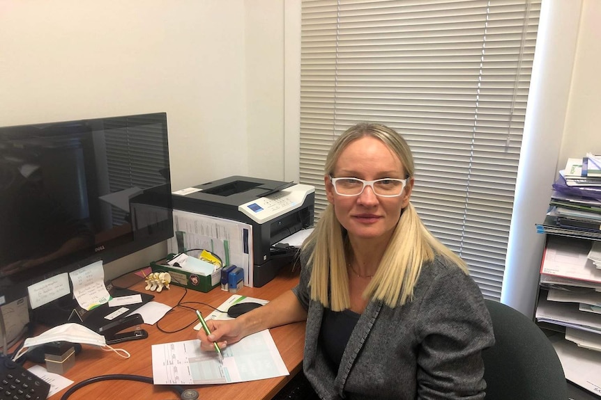 A blonde woman with white-rimmed glasses sitting at a desk.