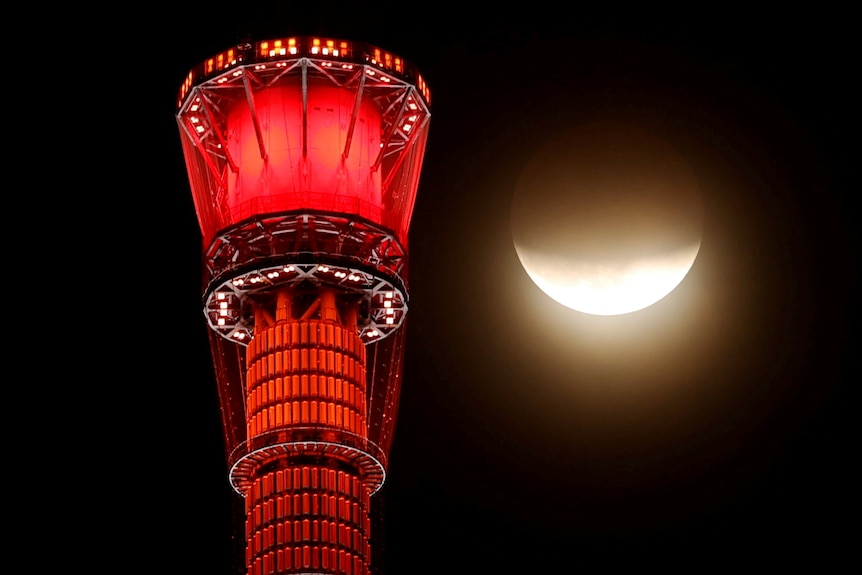 A bright yellow lunar eclipse beside a bright red tower in Tokyo