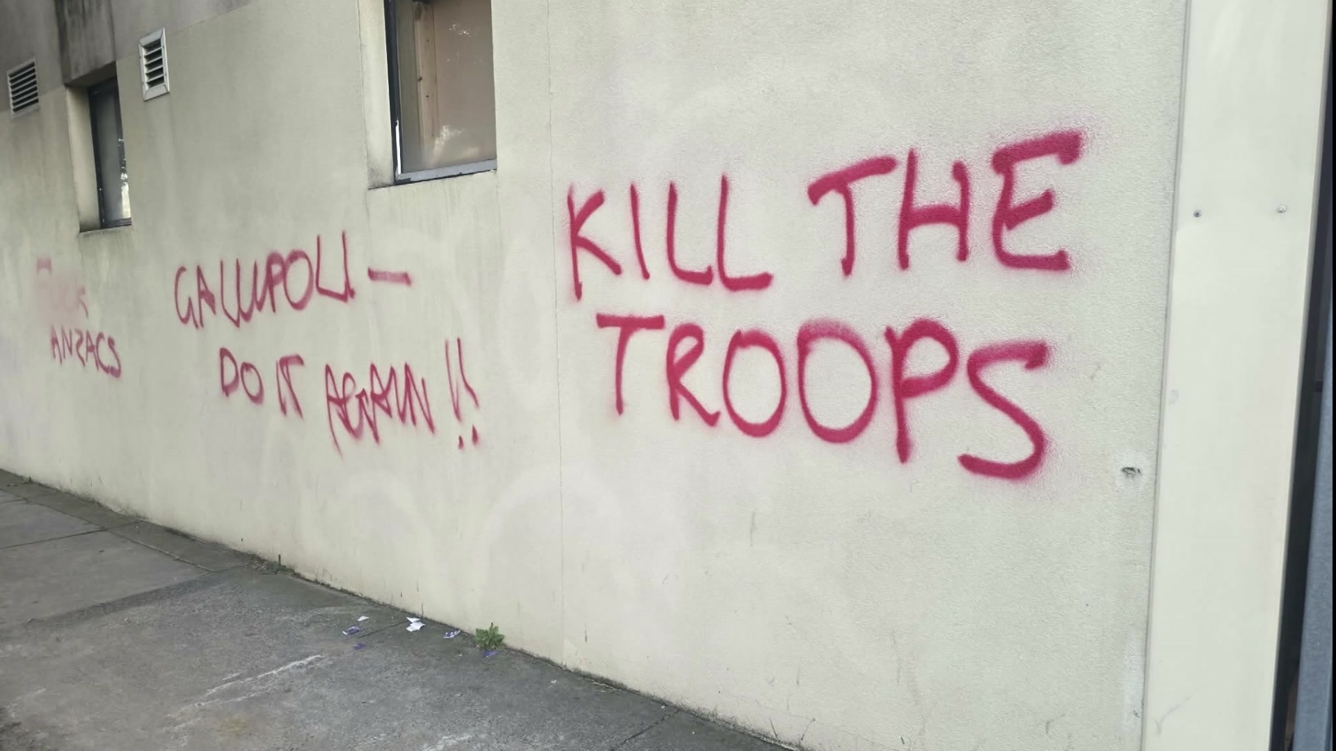 A white wall is spraypainted with red writing including "Gallipoli do it again" and "kill the troops".