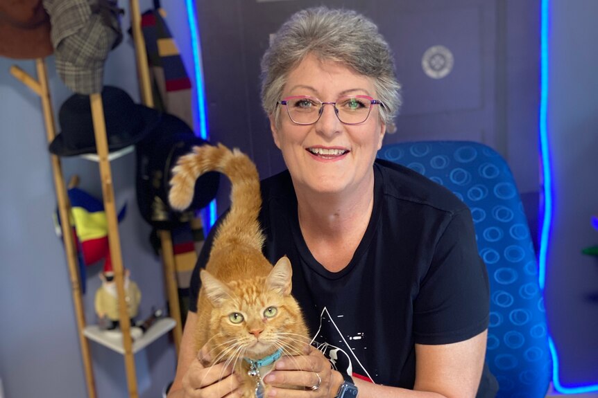 A smiling woman sitting at a desk with a small ginger cat