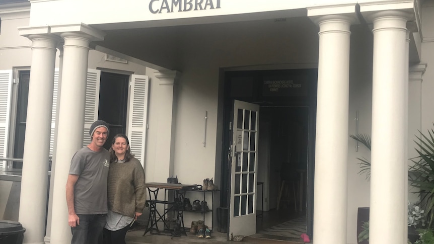 A man and a woman stand outside the a hostel they have purchased.