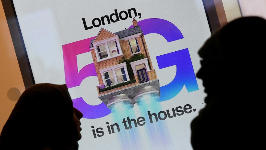 Pedestrians walk past an advertisement promoting the 5G data network at a mobile phone store in London.