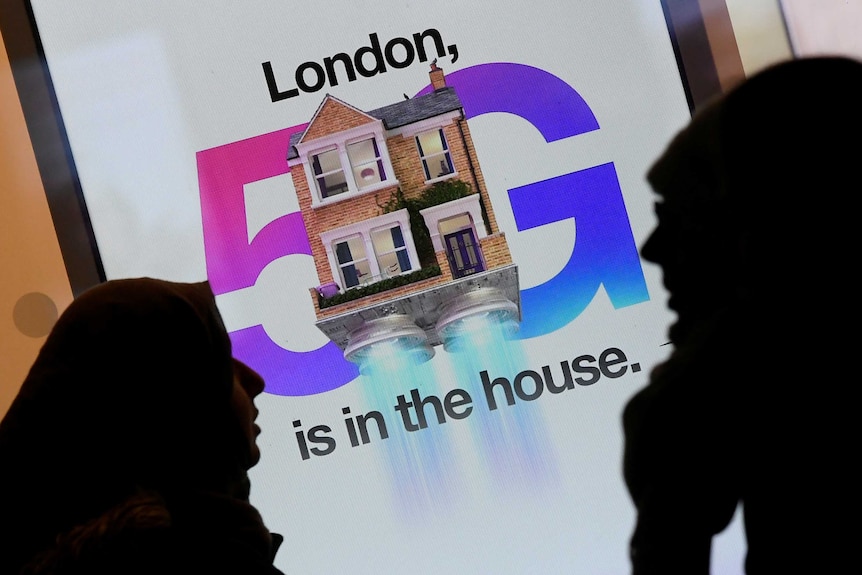 Pedestrians walk past an advertisement promoting the 5G data network at a mobile phone store in London.