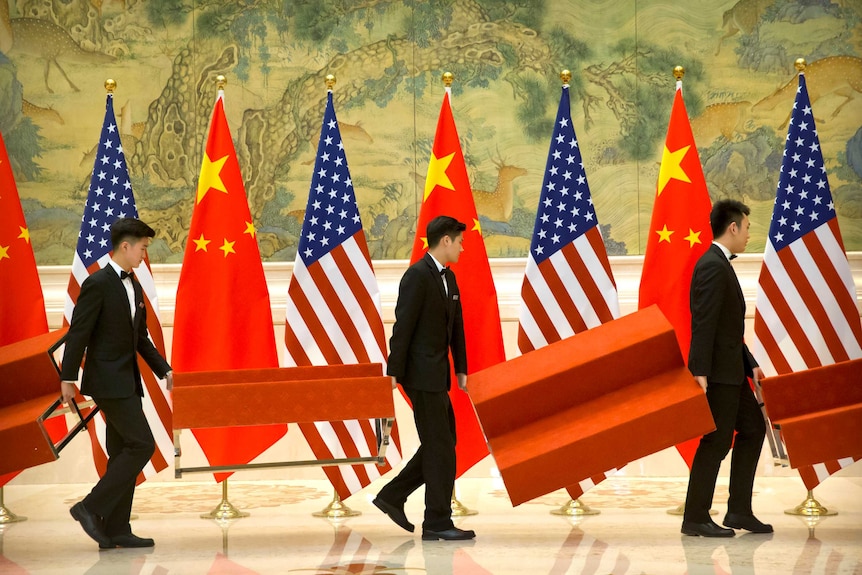 Men walk with pieces of furniture past Chinese and American flags.