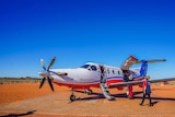Royal Flying Doctor Service plane on red dirt runway, being unloaded of medical supplies