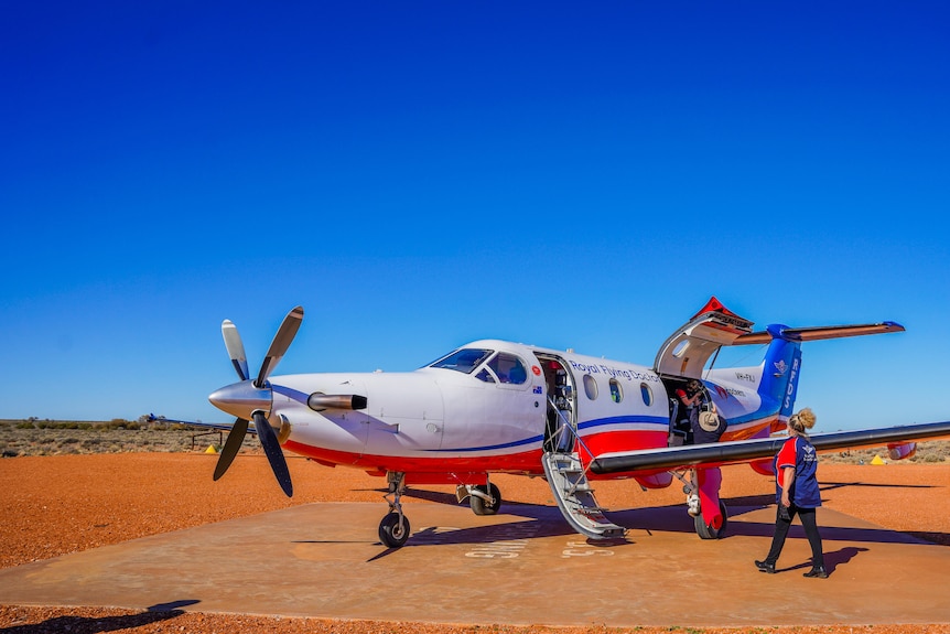 Royal Flying Doctor Service plane on red dirt runway, being unloaded of medical supplies