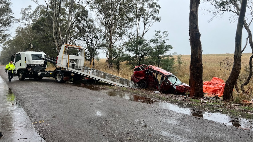 A red car extensively damaged in a crash is loaded onto a truck on a rainy day.