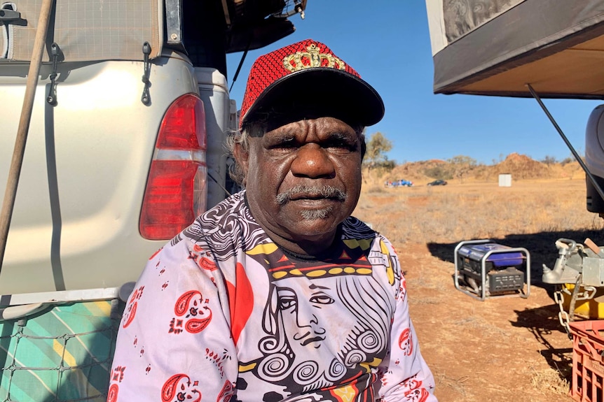 A portrait of an Indigenous man standing in front of a building outside.