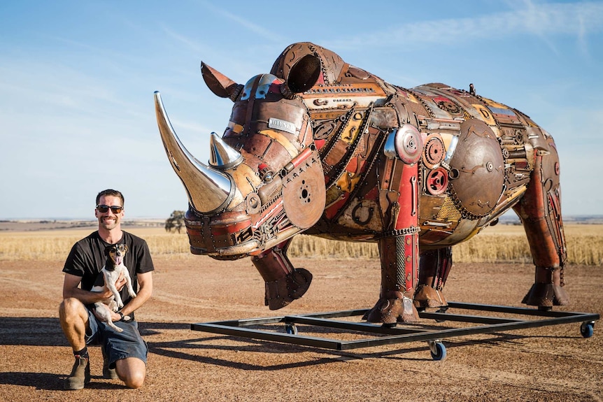A man with his dog and a giant metal rhino.