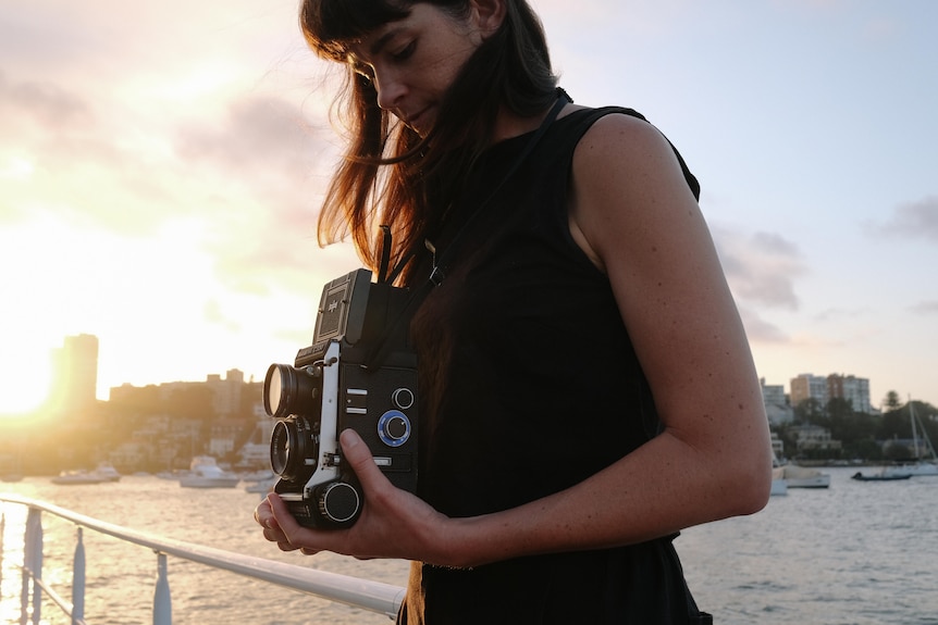 Artist Sammy Hawker photographs on a medium format camera next to Sydney Harbour at sunset