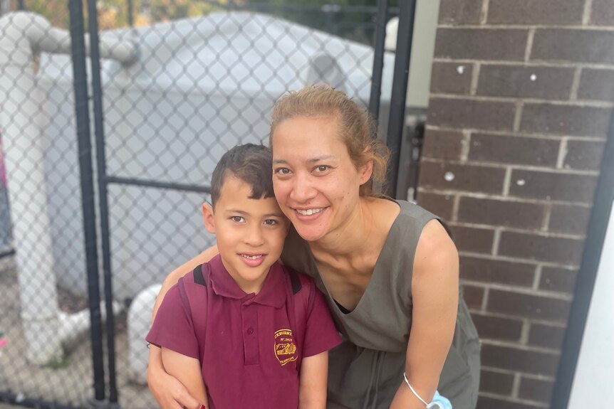 A primary school student in a uniform and his mum smile for the camera.